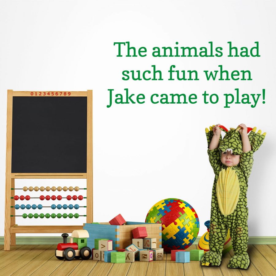 Personalised jungle quote wall sticker, jungle wall stickers. This sticker is in green text saying "The animals had such fun when Jake came to play!" The sticker has been placed in a playroom scene next to a small blackboard and above a child in a dinosaur costume.