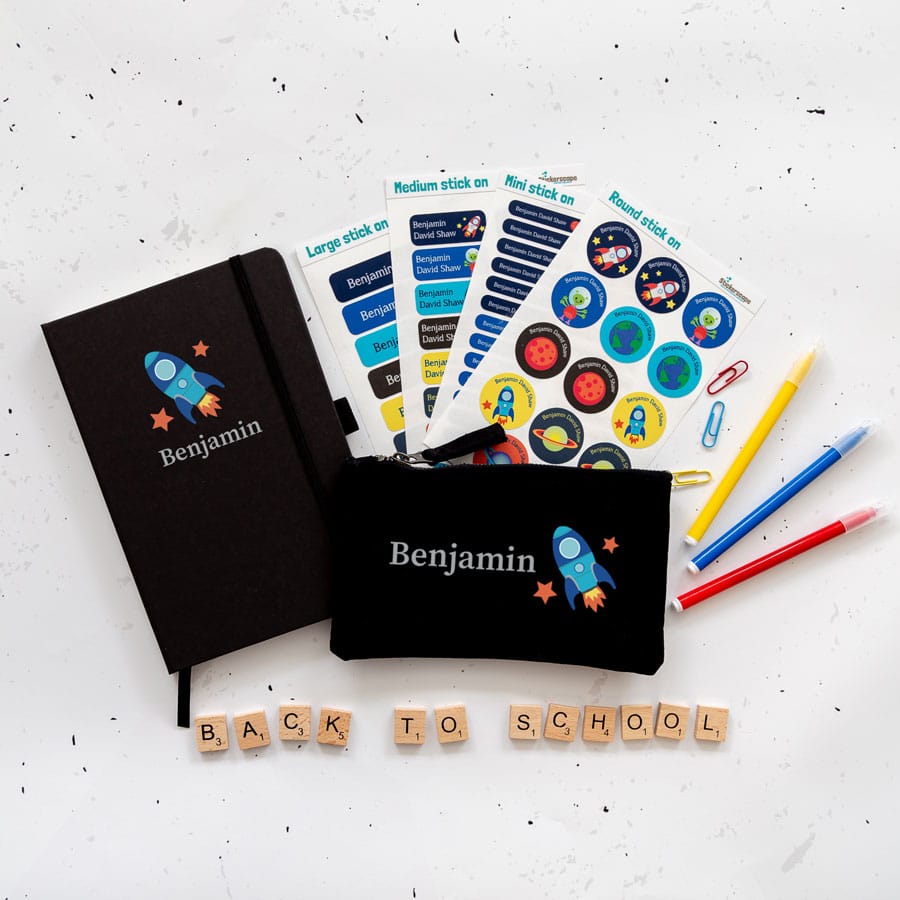 Space Back to school Mega Bundle. Featuring a black notebook with the name Benjamin in grey with a blue spaceship below. A black pencil casewith the name and the spaceship to the right. And four sheets of stick on name labels.