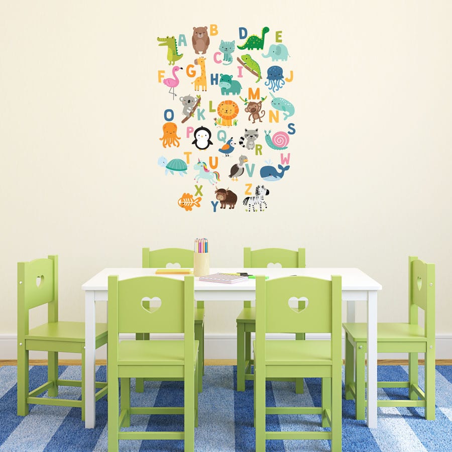 Jungle Alphabet Wall Sticker, jungle wall stickers. Image shows a colourful alphabet sticker arranged in a rectangular format with lots of animals. The sticker has been placed on a plain wall above a table with green chairs.