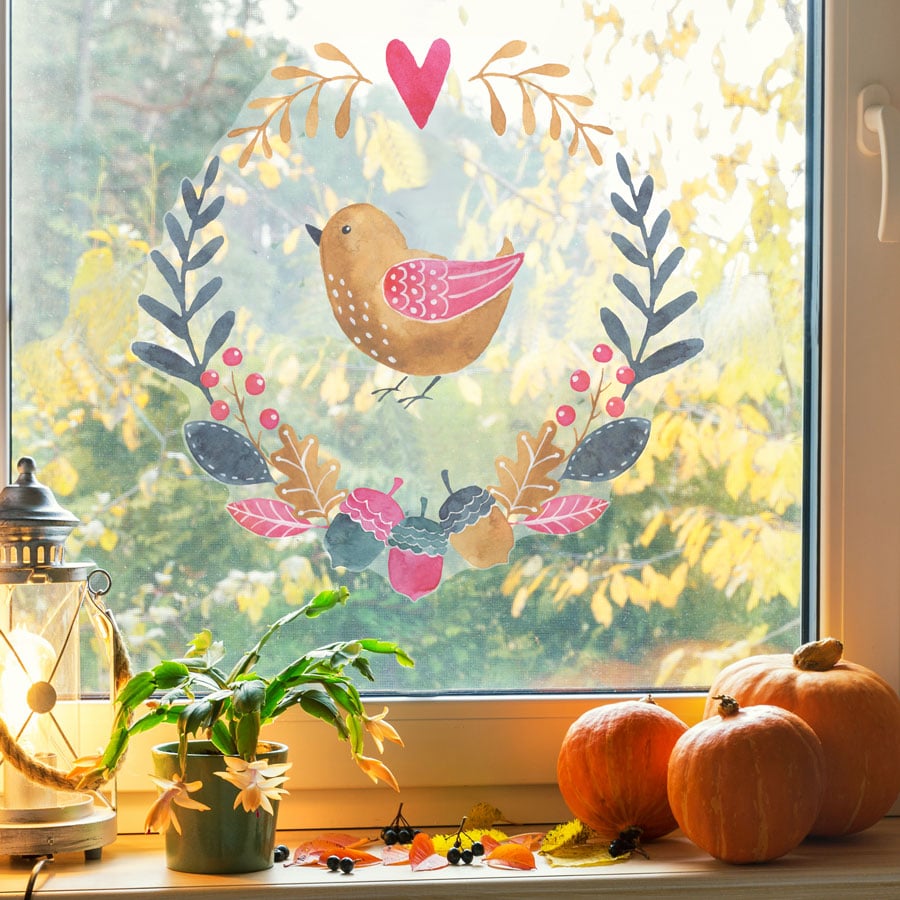 multicoloured woodland window sticker (Option 1), autumn window stickers. Gold bird in middle of a wreath made of blue, green and pink leaves and acorns with pink heart at the top.