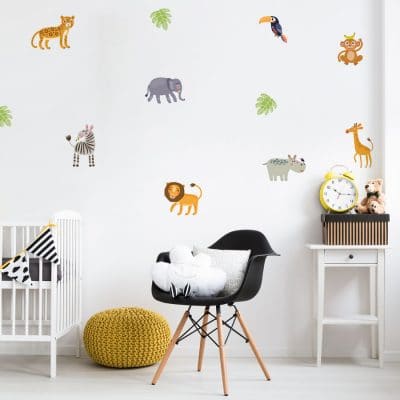 Jungle friends wall sticker pack, jungle wall stickers. The image features small lions, elephants, toucan, zebra, hippo, giraffe, monkey and cheetah as well as a couple of green leaves. These stickers have been placed on a wall in a nursery above a crib, a small black chair and a white table.