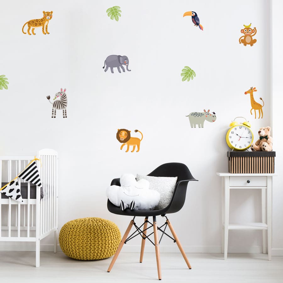 Jungle friends wall sticker pack, jungle wall stickers. The image features small lions, elephants, toucan, zebra, hippo, giraffe, monkey and cheetah as well as a couple of green leaves. These stickers have been placed on a wall in a nursery above a crib, a small black chair and a white table.