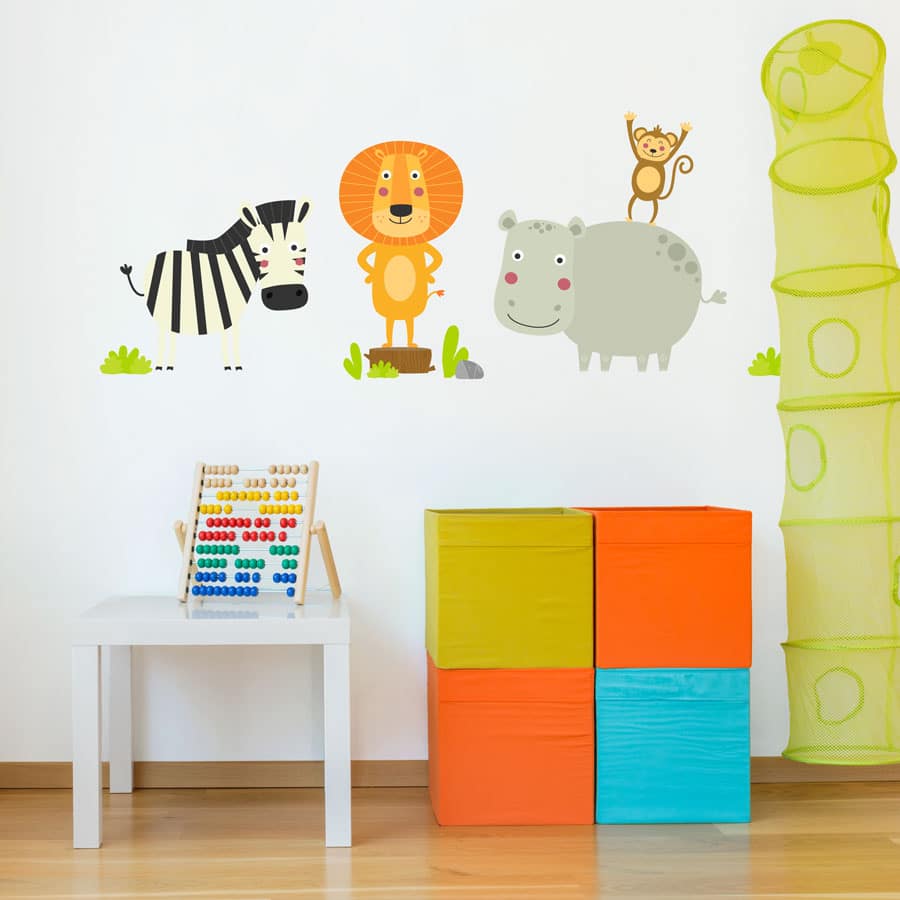 Cute jungle animals wall stickers. The image shows a zebra, a lion, a rhino and a monkey amongst some shallow grass. The sticker has been placed on a wall in a playroom above a small white desk and a colourful set of boxes.