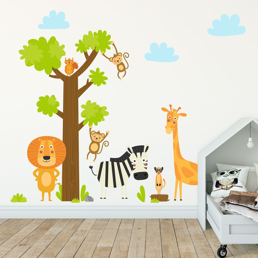 Jungle scene wall sticker pack. Shown in image is a large brown and green tree with two monkeys hanging off the branches and a squirrel at the top. There are also three blue clouds at the top. On the bottom of the sticker there is a lion stood on its back legs, a zebra a giraffe and a meerkat as well as a couple of small grass patches. The sticker has been placed on one wall next to and behind a child's bedframe.