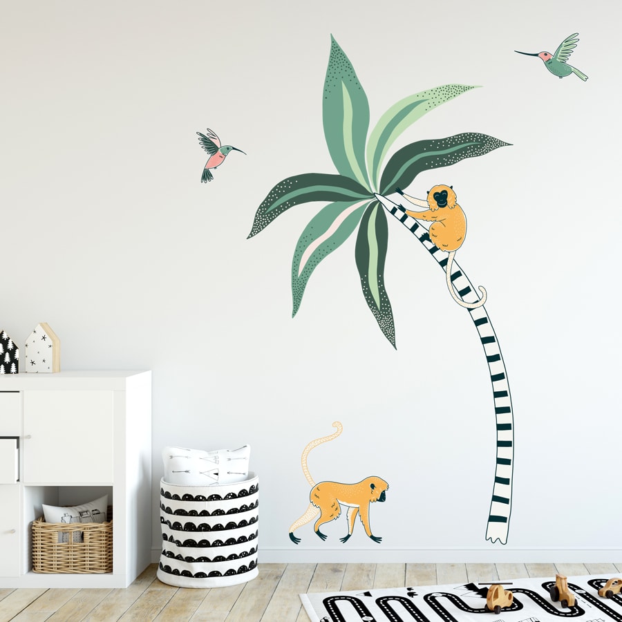 Tropical Palm And Monkeys Wall Stickers. Image displays a room with a large stripy palm tree sticker with green leaves, a yellow monkey on the tree and one walking along the ground, and two pink and green humming birds on the wall.