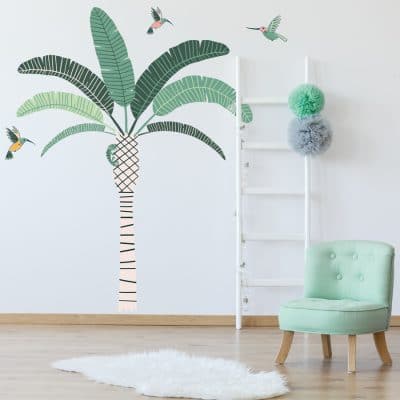 Tropical Palm Tree Wall Sticker Jungle wall sticker. Image showing a room with a green chair and a white rug and a stripy palm tree with green leaves and green and pink hummingbirds stickers on the wall.