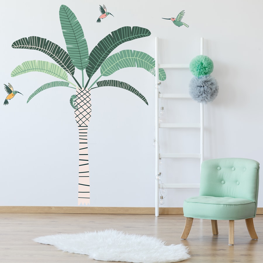 Tropical Palm Tree Wall Sticker Jungle wall sticker. Image showing a room with a green chair and a white rug and a stripy palm tree with green leaves and green and pink hummingbirds stickers on the wall.