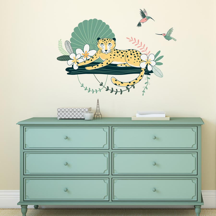 Cheetah and hummingbirds wall sticker pack, jungle wall stickers, safari wall stickers. Featuring a cheetah relaxing on a branch with flowers and green plants around. There is also to pink and green coloured humming birds. Jungle wall sticker is displayed above a light green set of drawers.