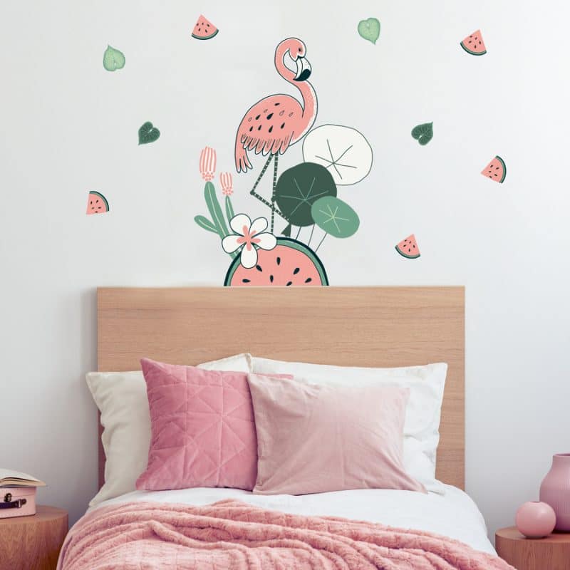 Flamingo and Watermelon jungle wall stickers. Features a pink flamingo standing on a large watermelon with a cactus and other plants around. Smaller pink and green watermelon slice stickers are positioned around. Stickers are placed above a pink bedspread.