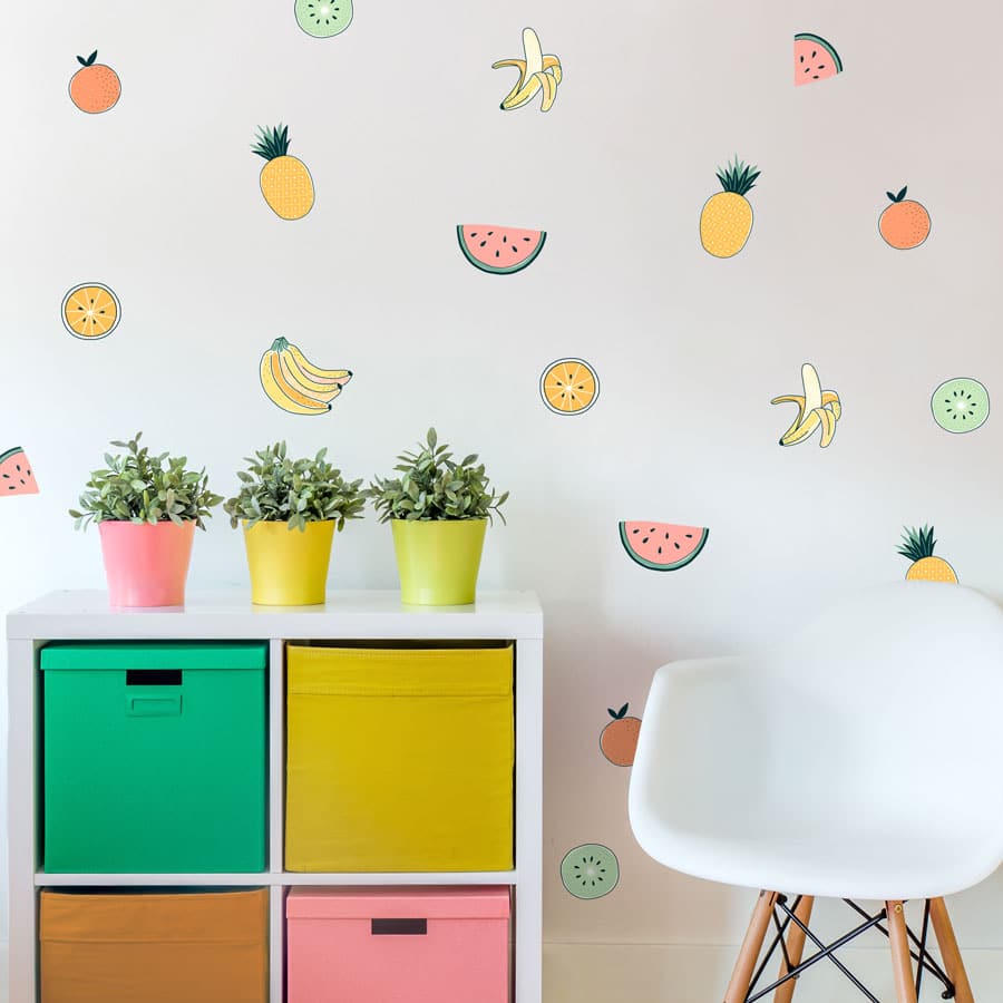 Tropical Fruit wall stickers, jungle wall stickers. Image features tropical fruit stickers on wall around a small white chair and a white set of drawers with colourful potted plants on top.