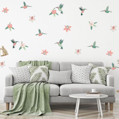 Hummingbird and Hibiscus jungle wall sticker pack. Image shows teal, green and pink hummingbirds and hibiscus flowers on wall around alight grey sofa with a sage coloured blanket.