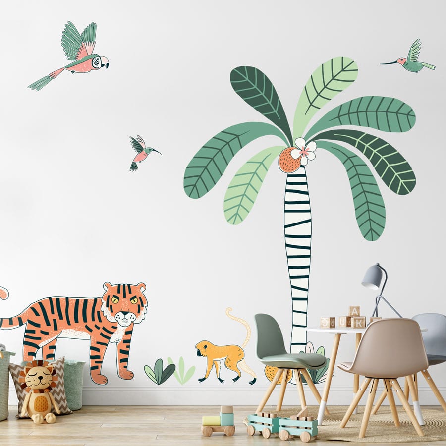 jungle wall sticker pack, jungle wall stickers. Image shows a large striped tree trunk with bright green leaves and coconuts, a tiger, monkey, a parrot and two smaller birds. The sticker has been placed on a light plain wall behind a set of small table and chairs.