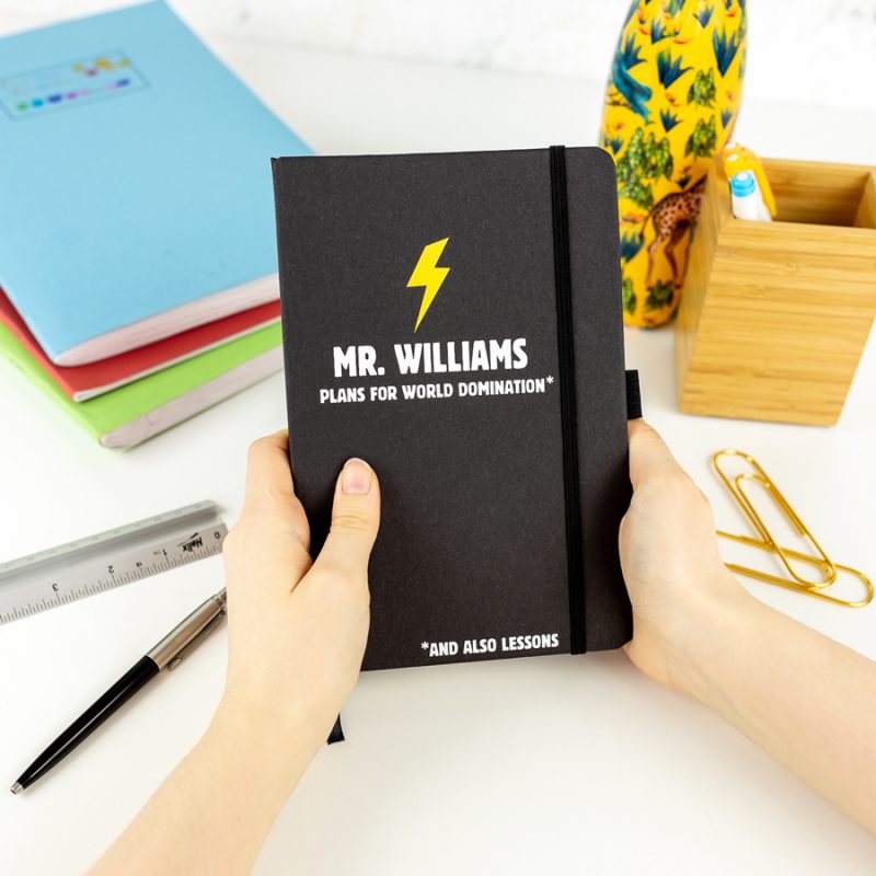Personalised world domination notebook in black features a yellow lightning bolt with a name of your choice and text 'plans for world domination' all in white and is a perfect gift for a teacher or teaching assistant to say thank you