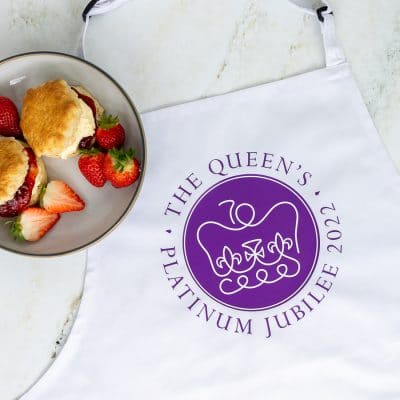 Official platinum jubilee logo apron shown flat with a plate of scones and strawberries