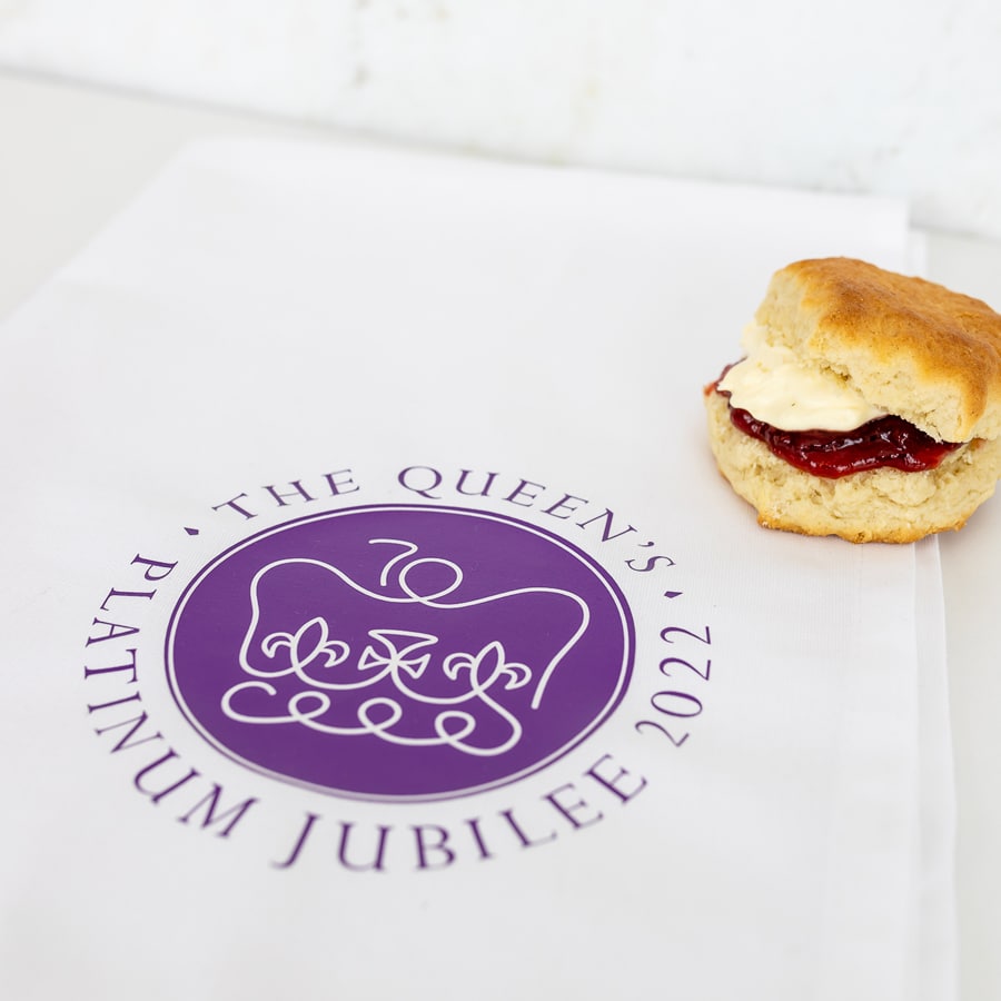 Official platinum jubilee logo tea towel shown flat with a scone