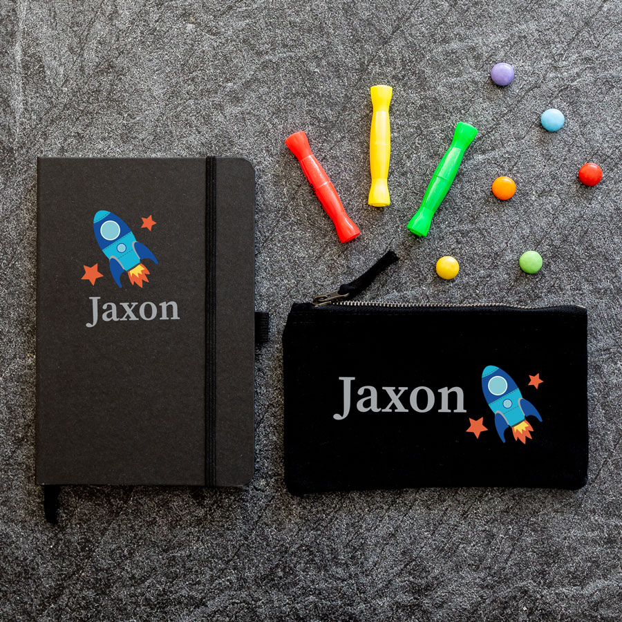 Mini space back to school bundle featuring a black notebook and black pencil case with the name Jaxon in grey with a blue spaceship to the right.