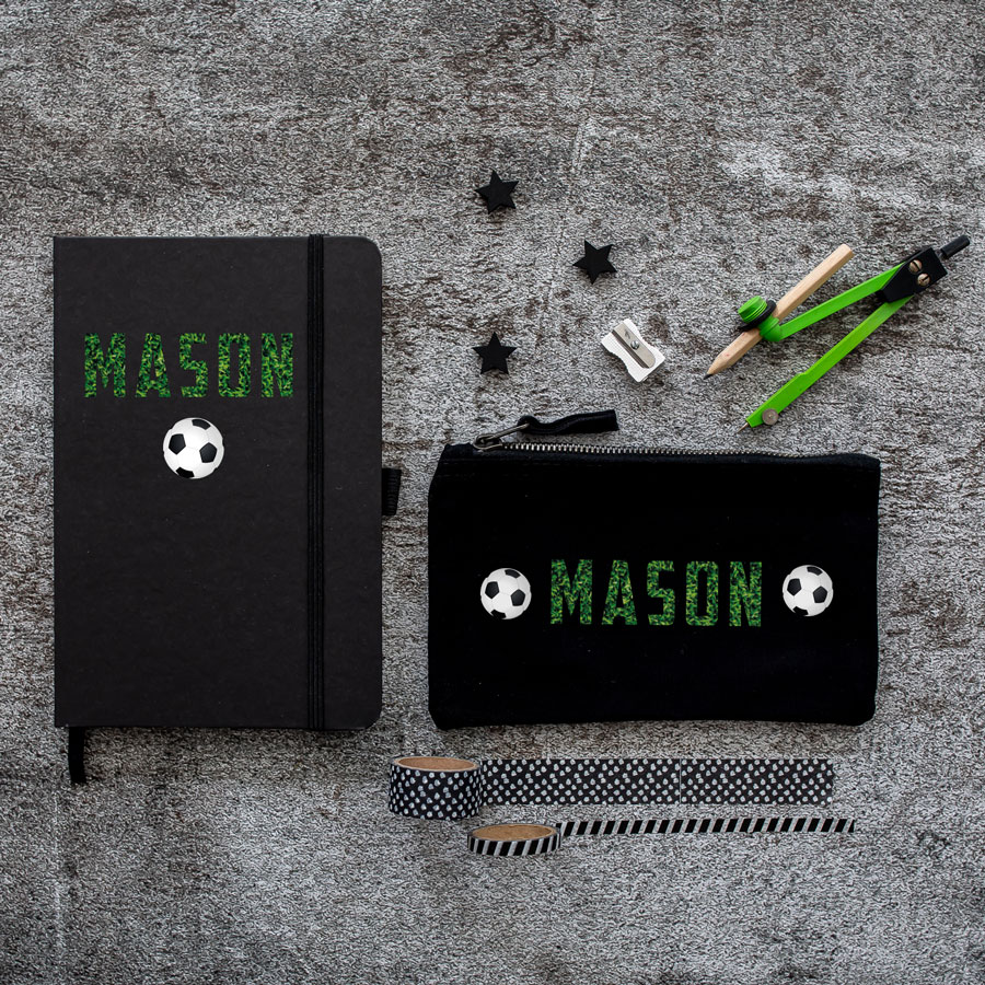 Mini back to school bundle featuring a black pencil case with the name Mason in a grass print between two footballs and a black notebook with the name Mason in a grass print above a football.
