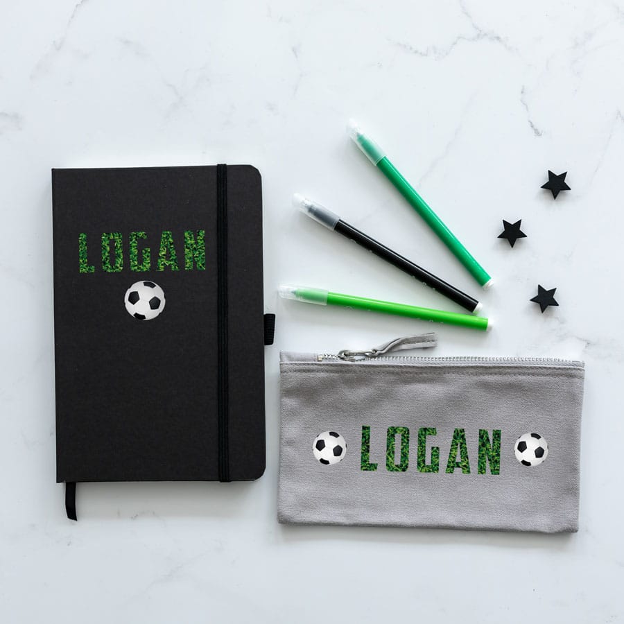 Mini back to school bundle featuring a grey pencil case with the name Logan in a grass print between two footballs and a black notebook with the name Logan in a grass print above a football.