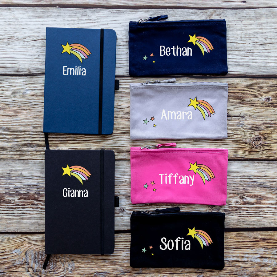 colour options for rainbow shooting star back to school bundles. black/blue notebook with rainbow shooting star image above name text in white. navy/grey/pink/black pencil case with white name text in centre, shooting star to top right and three stars bottom left.