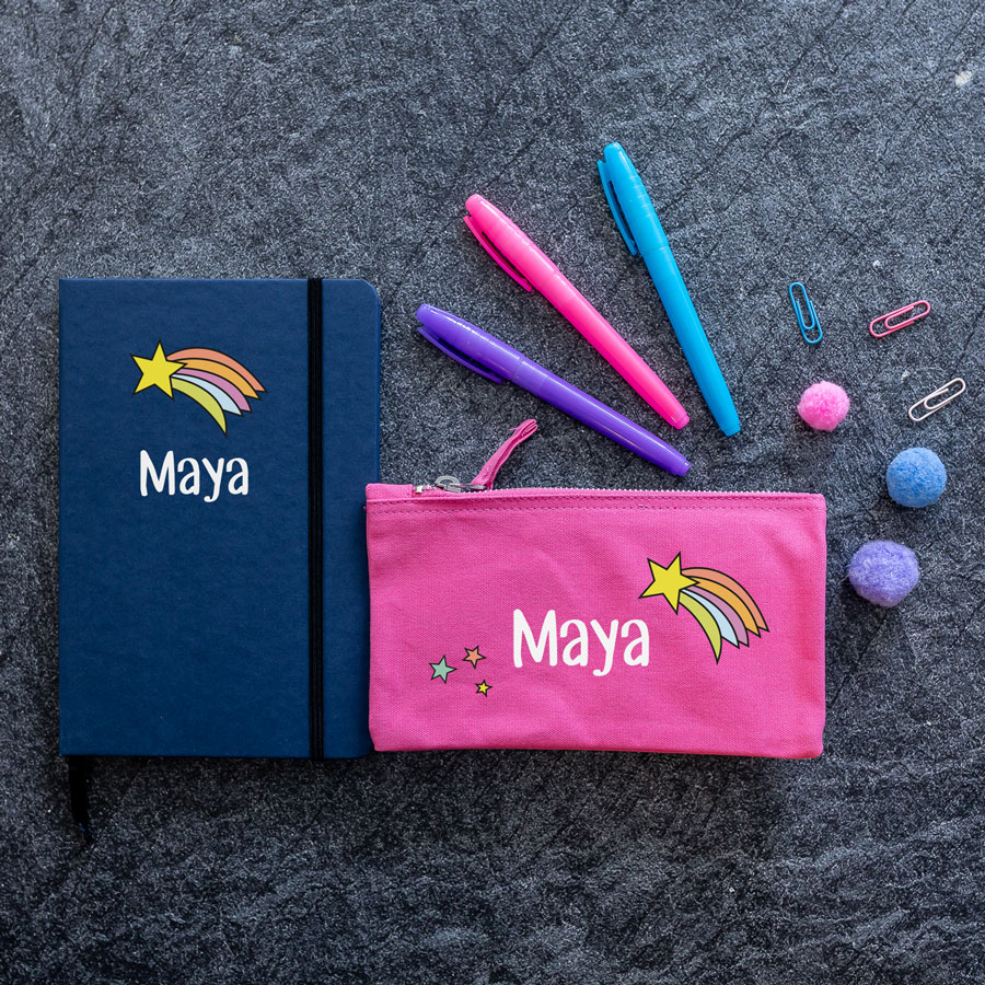 rainbow shooting star back to school mini bundle. blue notebook with rainbow shooting star image above name text in white. pink pencil case with white name text in centre, shooting star to top right and three stars bottom left.