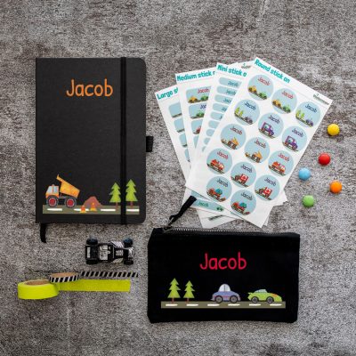 transport back to school mini bundle. black notebook with lorry and trees on road along bottom and text name in orange at top centre. black pencil case with road scene at bottom with car and trees and name text in orange or blue in centre. 4 sheets of stick on name labels.