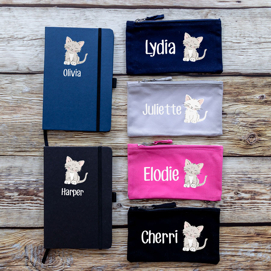 colour options for cat back to school bundles. blue/black notebook with cat illustration in centre with name text in white underneath. navy/grey/pink/black pencil case with image of cat in centre with name text in white to the left.