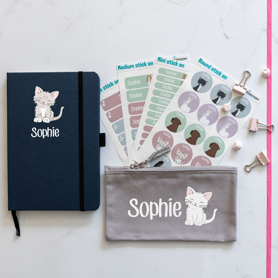 cat back to school mega bundles. blue notebook with cat illustration in centre with name text in white underneath. grey pencil case with image of cat in centre with name text in white to the left. 4 sheets of stick on name labels.