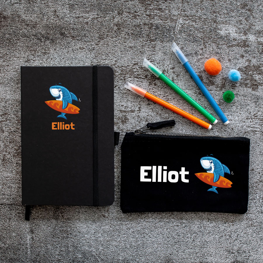 Little Shark back to school mini bundle. Black pencil case and black notebook. Image of blue shark holding orange surf board with name text underneath.