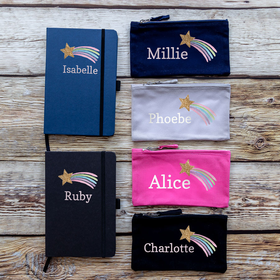 Shooting star back to school mega bundle colourways. Featuring a blue notebook and a black notebook. A navy pencil case, grey pencil case, pink pencil case and a black pencil case. All with name sin white and a pastel coloured shooting star with a gold glitter effect.