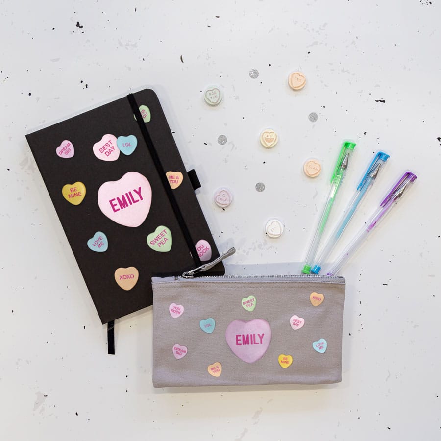 Love hearts back to school mini bundle. Image showing black note book and grey pencil case, both with name in dark pint text inside a large light pink heart surrounded with pastel coloured smaller hearts with positive words and phrases inside.