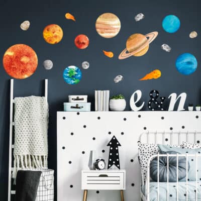 Watercolour-style solar system wall stickers featuring planets, the sun, moon, asteroids, and comets on a dark blue wall in a modern nursery or kids' bedroom