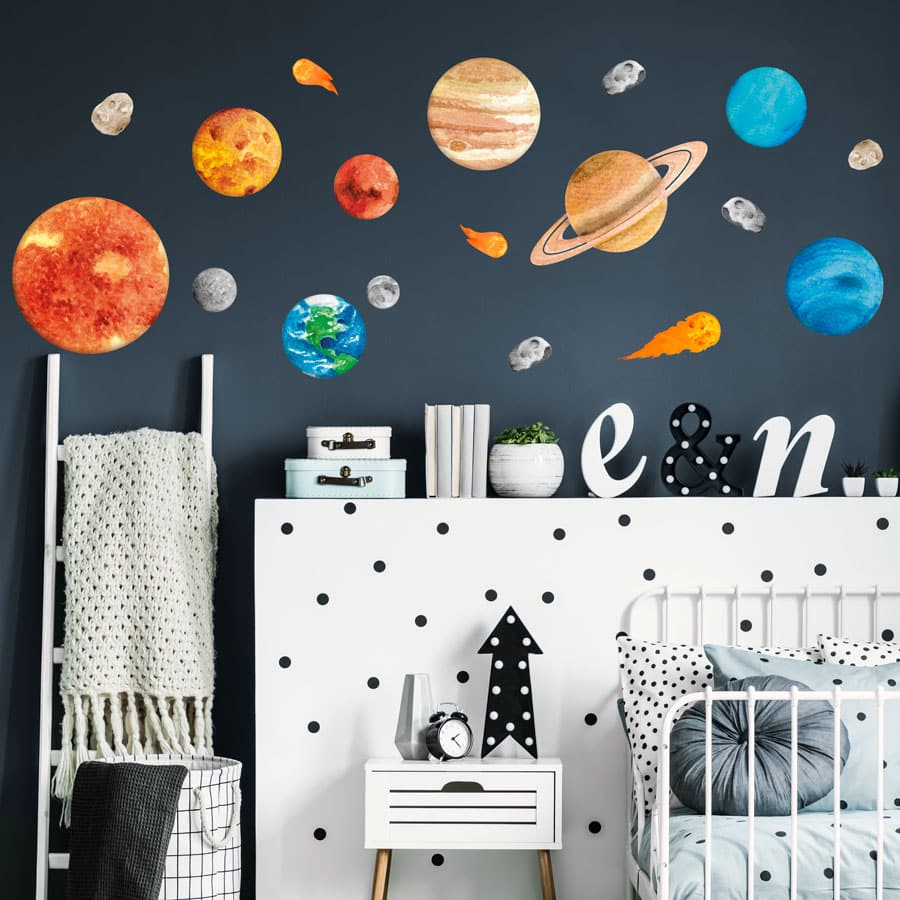 Watercolour-style solar system wall stickers featuring planets, the sun, moon, asteroids, and comets on a dark blue wall in a modern nursery or kids' bedroom