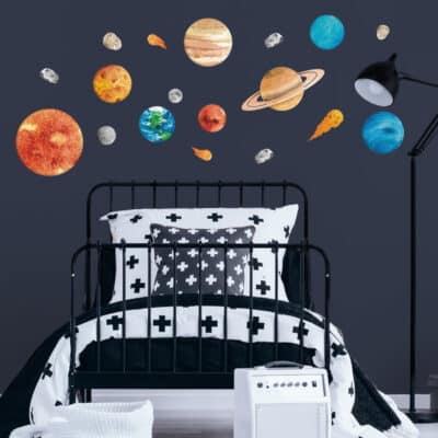 Watercolour-style solar system wall stickers featuring planets, the sun, moon, asteroids, and comets on a dark blue wall in a modern nursery or kids' bedroom