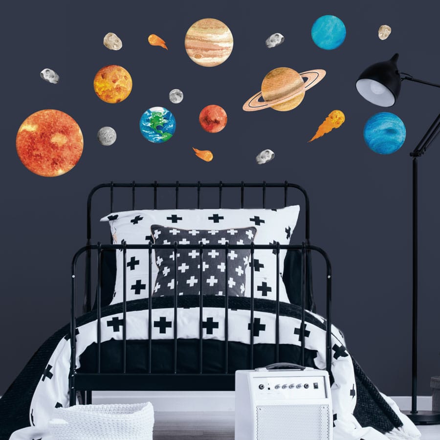 Watercolour-style solar system wall stickers featuring planets, the sun, moon, asteroids, and comets on a dark blue wall in a modern nursery or kids' bedroom