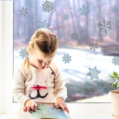snowflake window stickers (blue and grey) on a window with child and a winter garden in the background