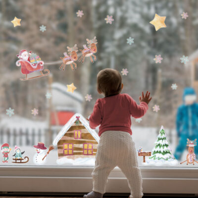 North Pole Christmas Window Stickers (Large size) on a window with baby standing by glass featuring Santa, Snowflakes and other festive elements