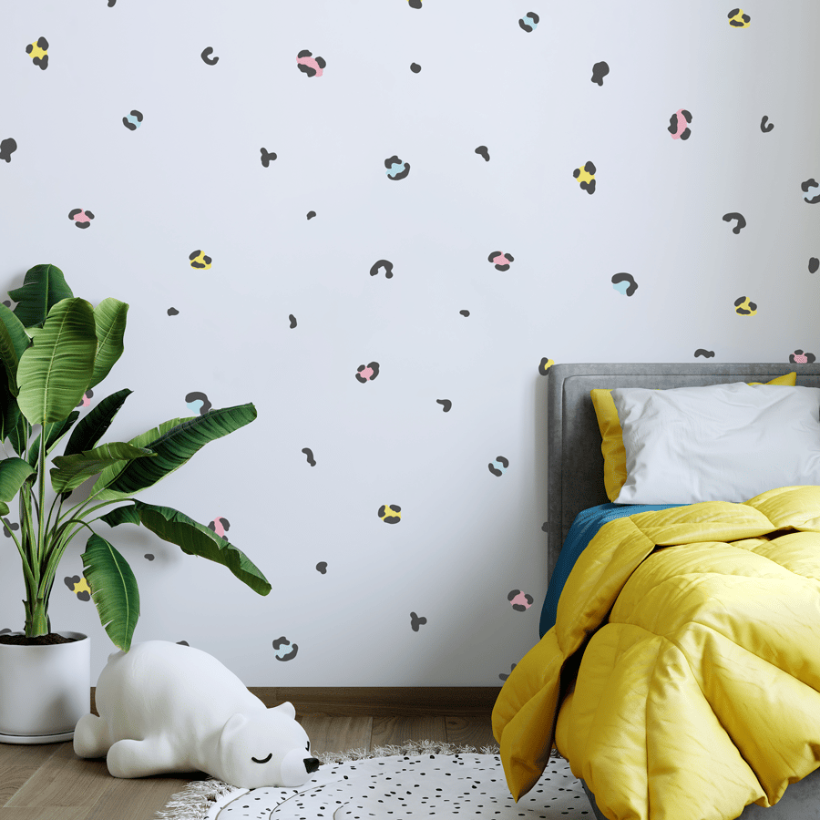 Colourful leopard print wall stickers in black and pastels shown on a white wall behind a yellow and blue bed and white potted plant