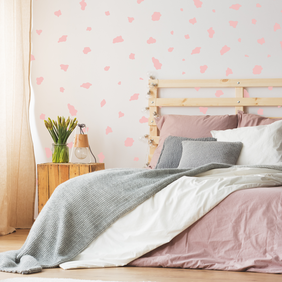 cow print wall sticker pack in pink shown on a white wall behind a wooden bed with pink and grey sheets