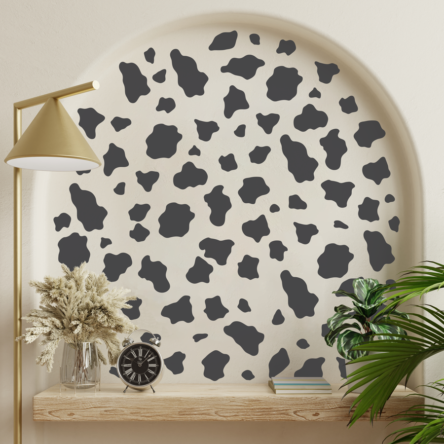 cow print wall sticker pack in brown shown on a warm white wall nock behind a gold lamp and green plants