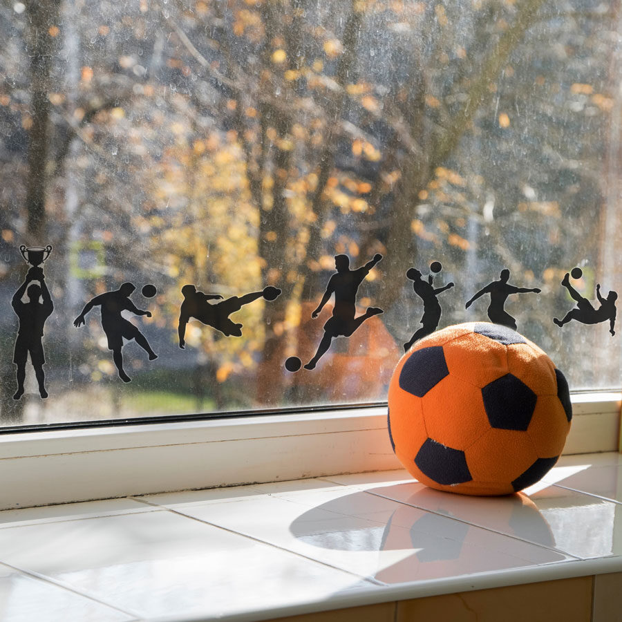 Football silhouette window sticker pack shown on a window in front of trees behind a orange football om=n a window ledge