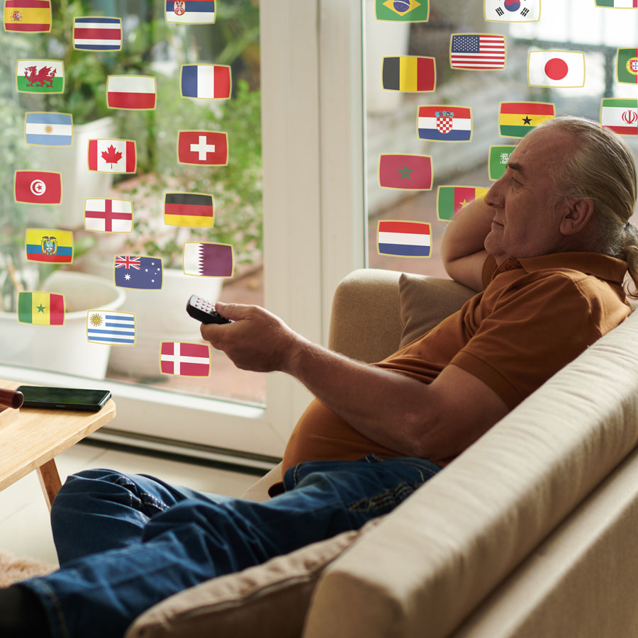 football tournament flags window stickers shown on a window behind a man sat on a sofa watching tv