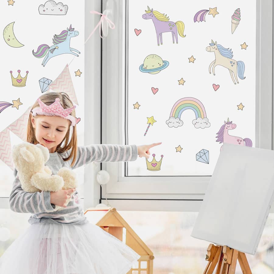 Colour-in Unicorn Window Sticker Pack shown on a window behind a young girl in a crown with a plush unicorn