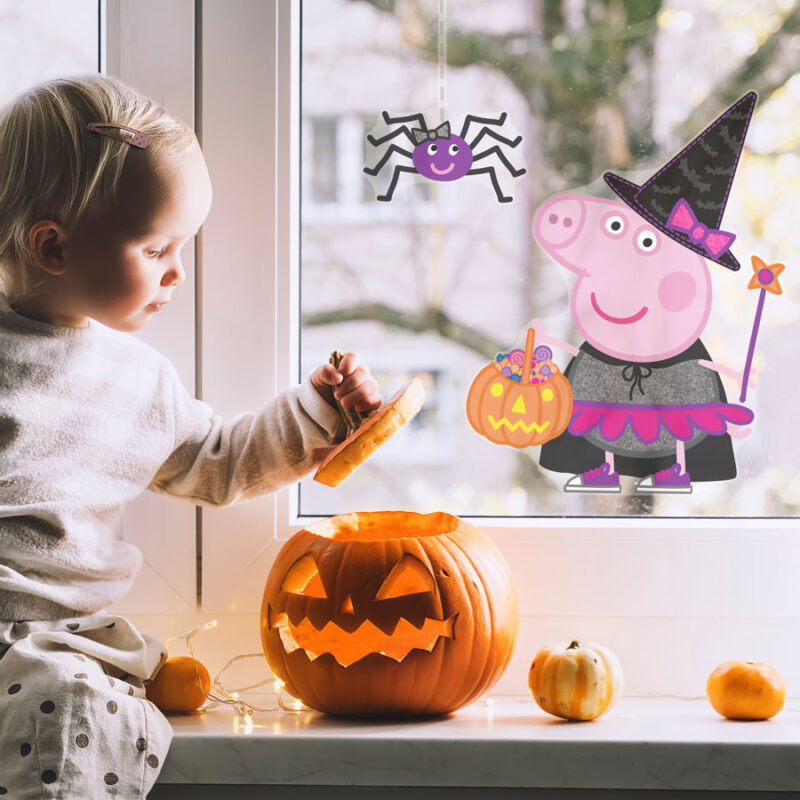 peppa pig witch window sticker shown on a window behind a carved pumpkin and small child
