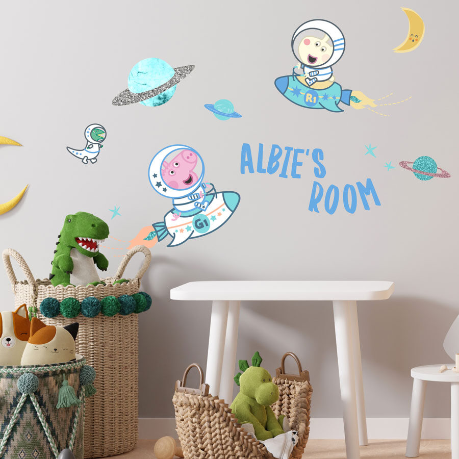 personalised george in space wall stickers shown on a light grey wall above a white table next to baskets holding childrens toys