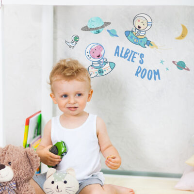 personalised george in space wall stickers shown on a light grey wall shown on a grey wall behind a small child