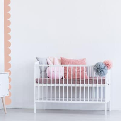scallop wall stickers in light pink going down a white wall alongside a white cot