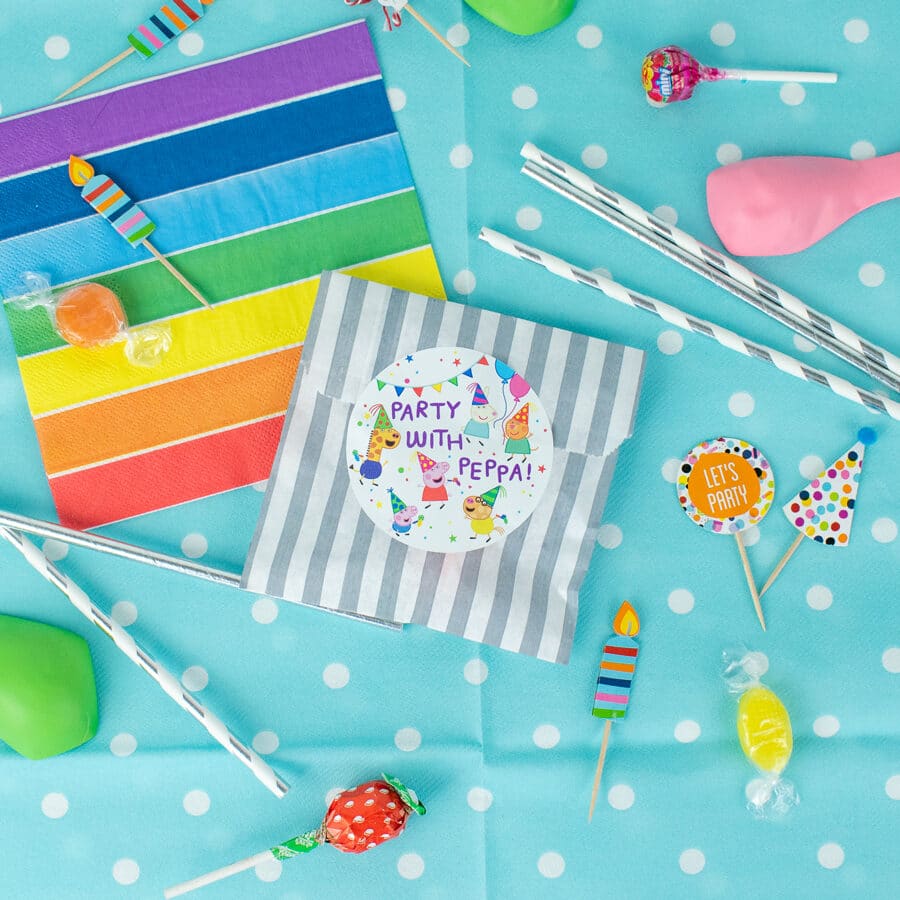 Peppa pig party bag label pack in white shown stuck to a striped party bag on a blue table cover