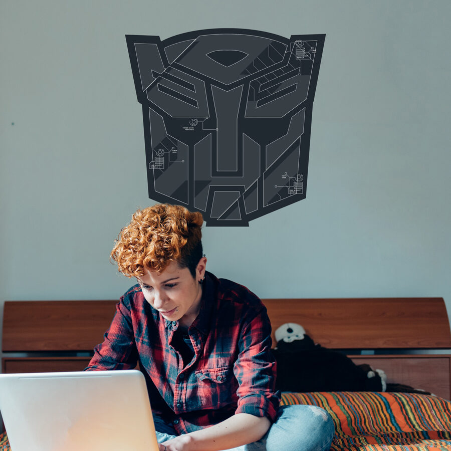 Grey Autobots Wall Sticker Pack shown on a grey blue wall behind a boy working on a laptop