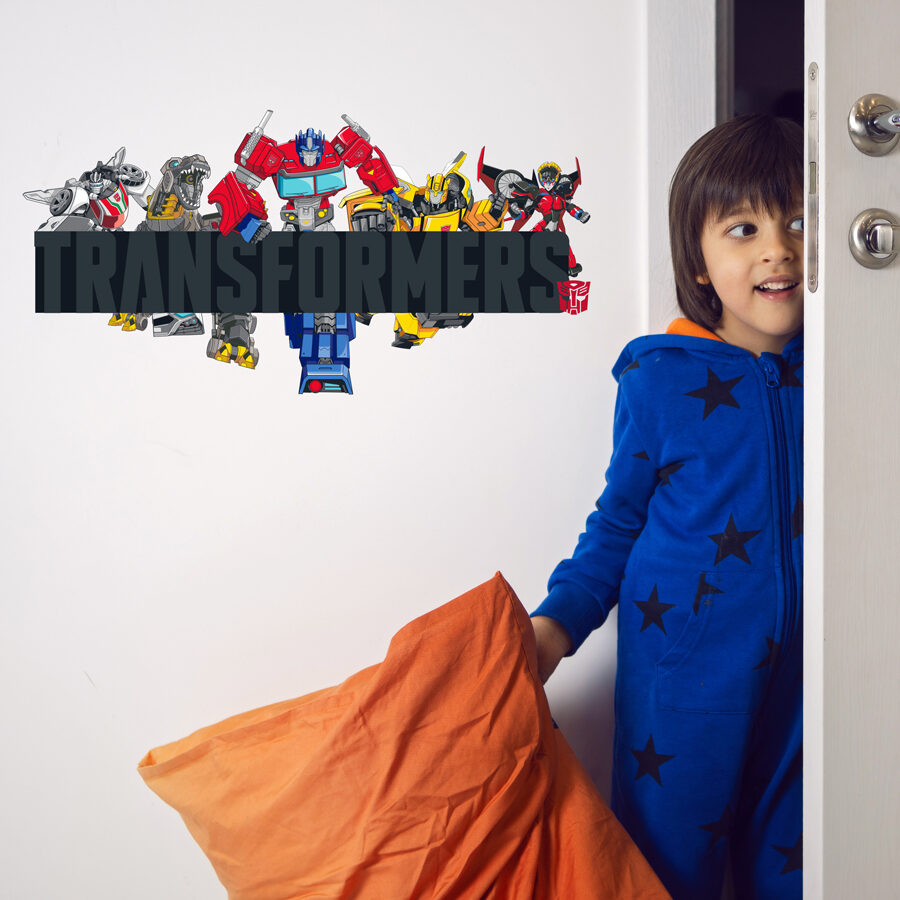 Transformers group wall sticker regular shown on a white wall behind a young boy in pyjamas