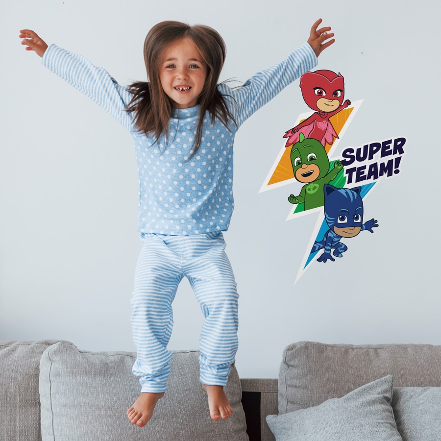 super team wall sticker shown on a grey wall behind s girl jumping on a sofa